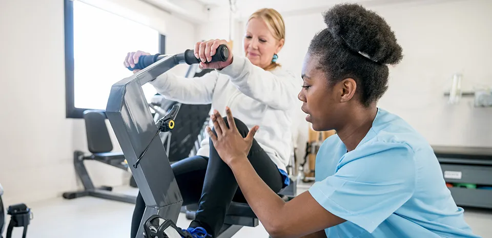 A nurse helps a patient on an exercise machine as part of her rehabilitation therapy.