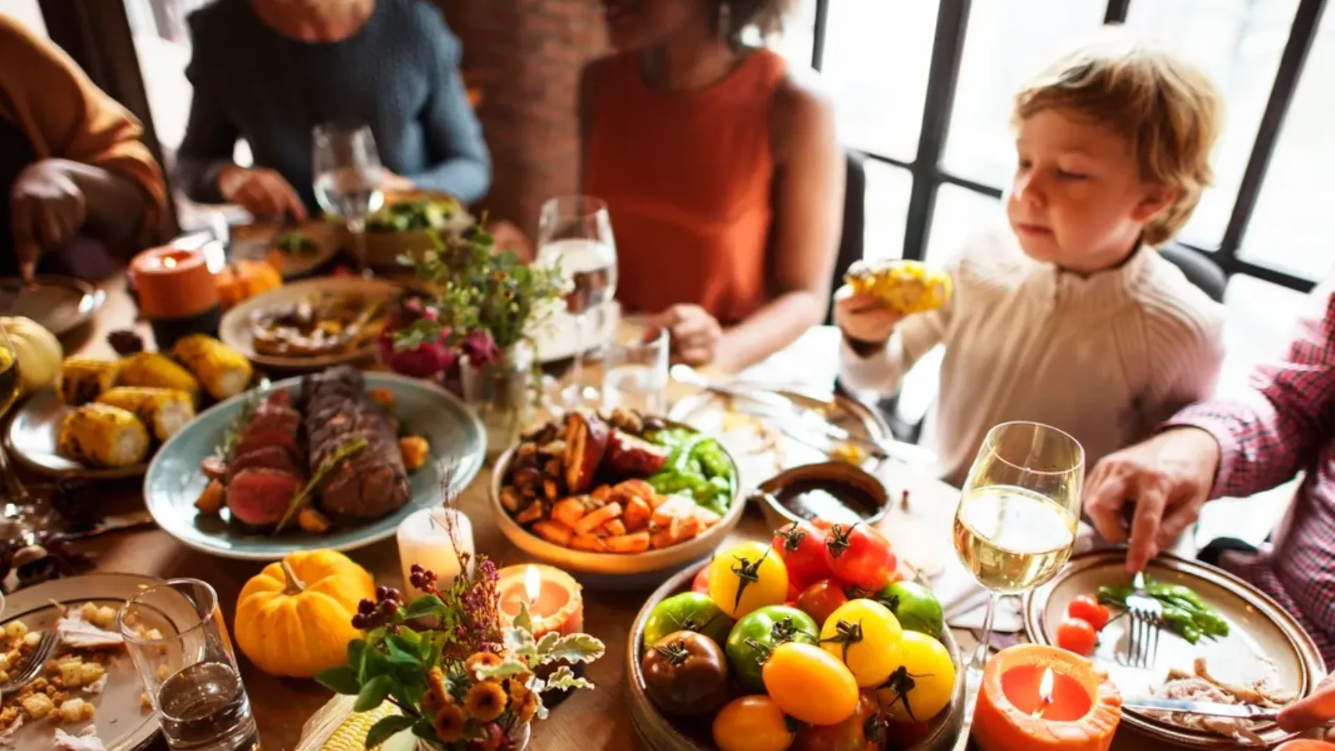 A child sits at a table full of food and people.