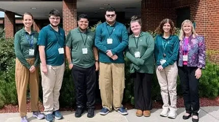 A group of teens who participate in Project SEARCH's internships poses together outside of a brick building.