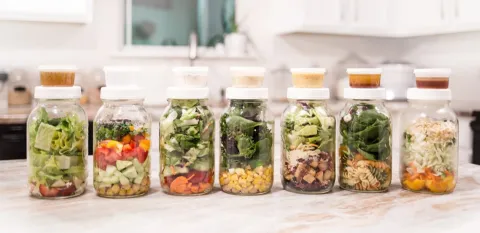 A set of mason jar salads with containers of dressing have been assembled on a countertop.