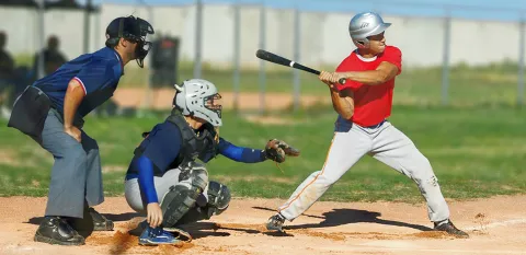 A batter is ready to swing at home plate with the umpire and catcher ready to participate in the play.