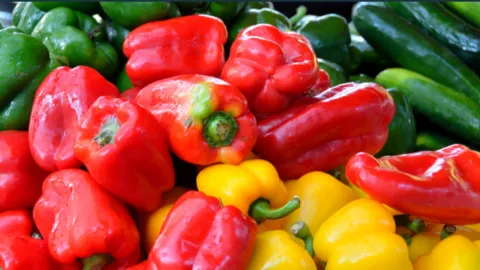 Red and yellow peppers are on a pile of other vegetables.