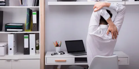 A worker at a desk is shown stretching from behind.