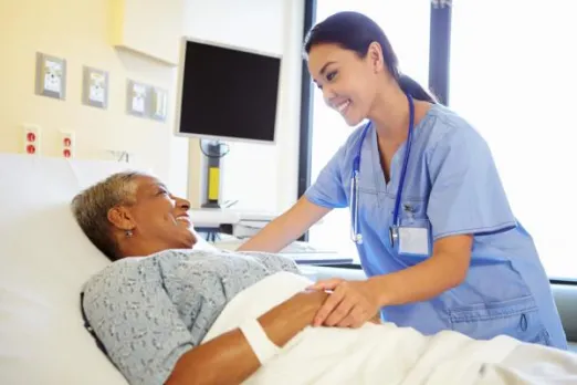 A nurse is comforting a woman in a hospital bed and they are both smiling.