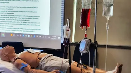 A medical mannequin and IV fluids are set up in the training room for paramedics learning to start antibiotics on-site.