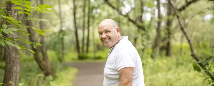 man in white t-shirt with thyroid issue walking on trail in woods