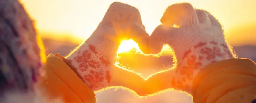 two hands making a heart shape towards towards in the sun in the winter time