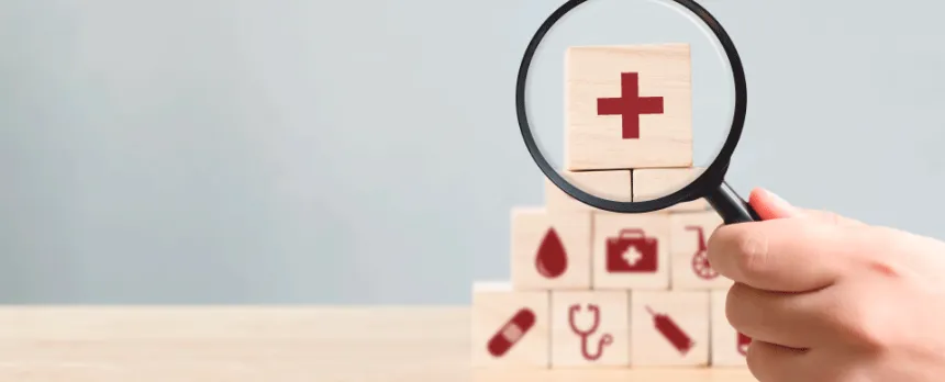 Medical icon blocks stacked in a pyramid, with a red cross at the top highlighted by a magnifying glass.